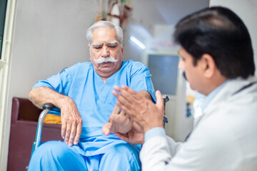 Indian male doctor check disabled elder patient sit on wheelchair at home hospital, paralyzed old...