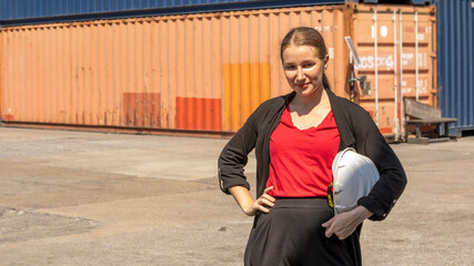 Young female manager with white hard had checks stock and containers in a shipyard or logistic storehouse  during a sunny day. Female clerk takes inventory in a factory