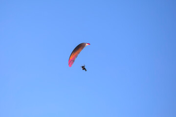 Paraglider in orange and pink colors with motor in front of a blue sky flying in the morning sun