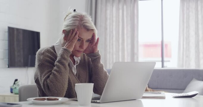 Tired senior woman with a headache looking at laptop screen sitting at desk feeling unhappy. Frustrated mature businesswoman made mistake in work, has issues with project. Stressing working from home