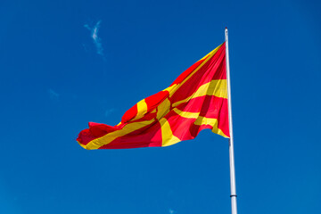 Flag of North Macedonia on blue sky. Stylised yellow sun on a red field on flag.