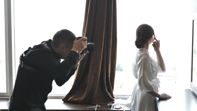The photographer takes a picture of a beautiful bride In a wedding dress by the window