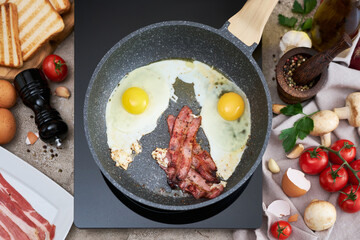 Frying eggs and bacon on a pan on induction hob at domestic kitchen