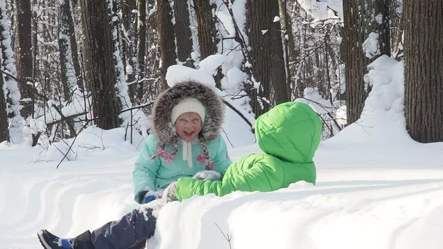 A family with children walks in the winter in the forest. Boy and girl on a walk in the forest or park. play, throw snowballs, wallow in the snow, snow angel. Holidays for Christmas, New Year.