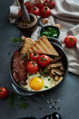 Fried eggs, bacon, tomato and toasted bread in a black ceramic pan at domestic kitchen