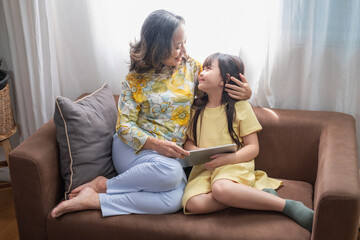 Portrait of an elderly woman and granddaughter reading tablet to enhance reading skills and family activities.