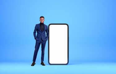 African businessman hands in pocket near phone, mockup display on blue background