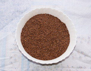 Flaxseeds or flax seed in a white bowl in white background.