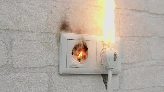 Electrical socket on fire in house on wall indoors close up. Short circuit, faulty wiring, voltage overload.