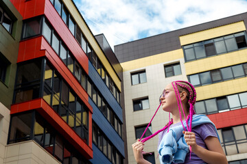 Portrait of a caucasian teenage girl with pink braids against the background of urban high-rise...
