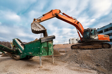 Fototapeta na wymiar Excavator loads soil in mobile crushing and sorting complex
