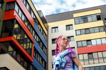 Portrait of a caucasian teenage girl with pink braids against the background of urban high-rise...