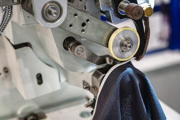 Machine sews cuff to dark blue fabric edge in workshop