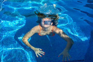 Young woman submerged under water in swimming pool. Coming to the surface. Blue background. Summer...