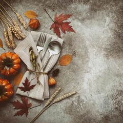 Thanksgiving autumn place setting with cutlery, decorative pumpkins and colorful leaves. Top view, flat lay. Square toned image.