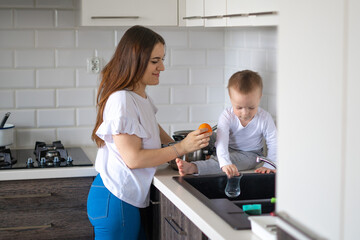 Happy mother with little boy cooking soup together in kitchen at home. Little baby boy is eating a green apple. Focus on woman