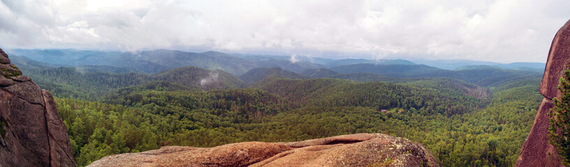 Panorama of hills covered with coniferous forest. Dramatic sky.