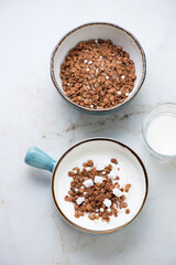 Turquoise bowls with greek yogurt and chocolate granola on a light-beige marble background, vertical shot, high angle view