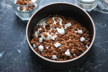 Bowl of chocolate granola with coconut and greek yogurt, middle close-up on a black marble background