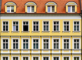 Geometrically strict yellow facade with uniformly arranged windows under a red tiled roof in...