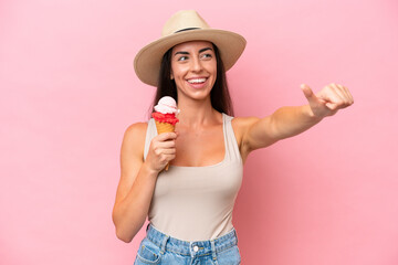 Young caucasian woman with a cornet ice cream isolated on pink background giving a thumbs up gesture