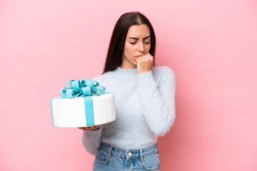 Young caucasian woman holding birthday cake isolated on pink background having doubts