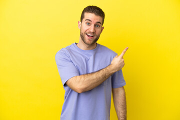 Handsome blonde man over isolated yellow background surprised and pointing side