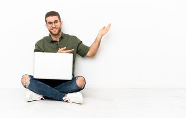 Young man sitting on the floor extending hands to the side for inviting to come