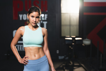 Obraz na płótnie Canvas Asian athlete woman in sportswear slim muscular body posing after exercise in gym.Portrait female workout bodybuilder with sweat showing abdominal muscles at sport club fitness.