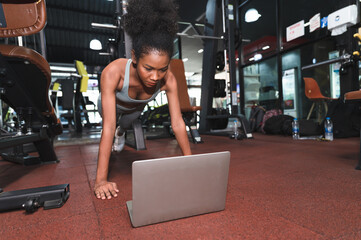 African American sport woman push ups with learning of notebook computer at fitness gym - Powered by Adobe