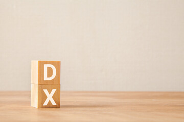デジタルトランスフォーメーション。DX。木製のブロックに描かれているDXの文字。木製のテーブルの背景。