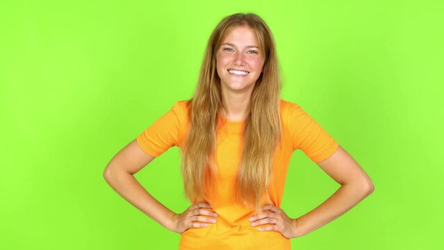 Young pretty blonde woman on green screen chroma key posing with arms at hip and laughing over isolated background