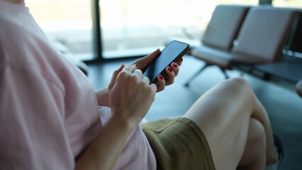 Woman traveler with smartphone in her hands sits in departure area at airport or train station