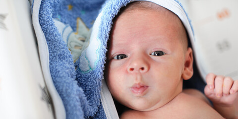 Close-up detail portrait of cute little peaceful newborn baby chield lies wrapped in a towel after a bath. Love and family emotion