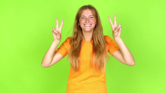 Young pretty blonde woman on green screen chroma key smiling and showing victory sign with a cheerful face over isolated background