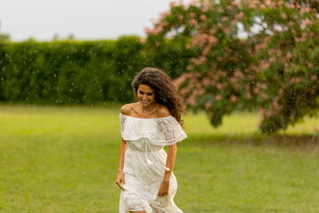 Fototapeta na wymiar Joyful young woman caught by the summer rain in the park