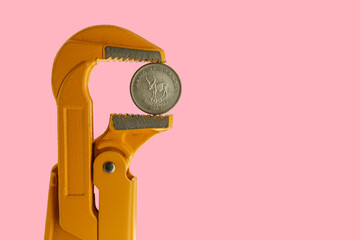 One hundred shillings Uganda coin held in an orange plumber wrench on a pink background