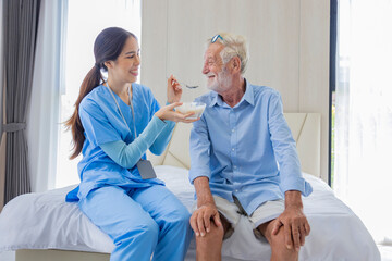 Hospice nurse is feeding porridge food to Caucasian man at pension retirement center for home care rehabilitation and post treatment recovery process