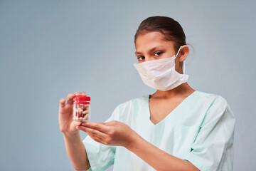 The girl is a young nurse or assistant in medical clothing and a mask holding a package of pills.