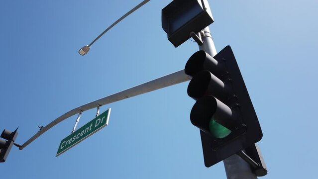 Los Angeles, California, USA, June 21, 2022: DOLLY SHOT - Modern traffic light at Santa Monica Boulevard with Crescent Drive Street sign above. Green traffic light in Beverly Hills.
