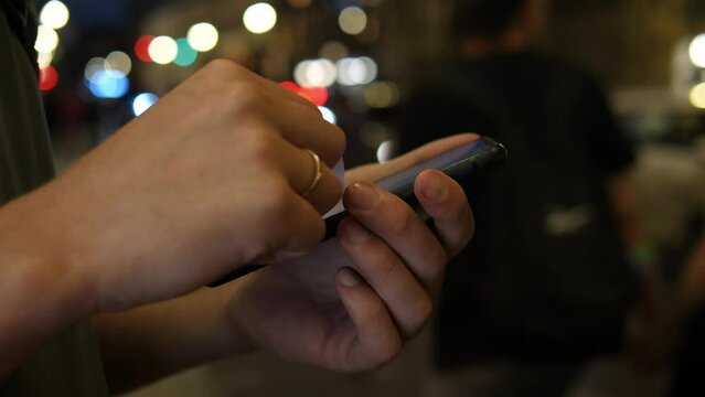 Close up of hands using smartphone at night on busy city street, concept of searching or using social network.