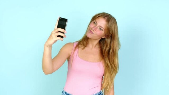 Young pretty blonde woman using mobile phone and doing a selfie over isolated background