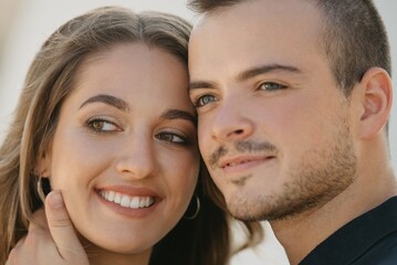 A close photo of a romantic guy who is holding his smiling girlfriend in the modern urban space at the sunset in a Spain town. A couple of tourists on a date in the evening in Valencia.
