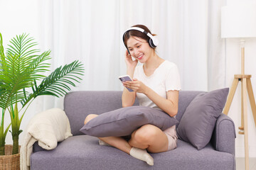 Obraz premium Lifestyle in living room concept, Young Asian woman in headphone to listening music on smartphone
