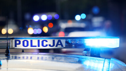 Akcja policji wieczorem w mieście. - Sygnalizator błyskowy niebieski na dachu radiowozu policji polskiej w nocy. - obrazy, fototapety, plakaty