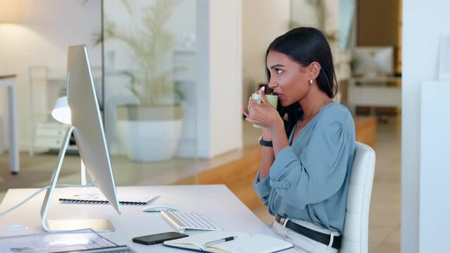 Female executive reading and typing an email to partners on a computer at work. Successful business woman chatting to colleagues while sitting in an office chair, drinking tea or coffee.