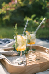 Glasses with delicious summer lemonade decorated with rosemary. Picnic blanket in nature.