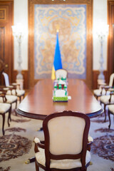 an empty chair at the head of the meeting negotiation table with the flag of Ukraine in the background out of focus