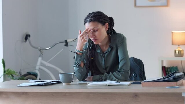 Frustrated, tired and worried woman struggling to deal with burnout, eye strain and problems with difficult deadlines. Stressed designer with a headache working on a digital tablet in a trendy office