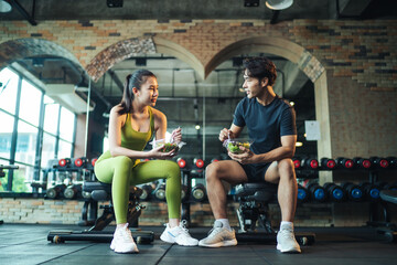Asian couple healthy eating salad after exercise at fitness gym. Asian man and woman eating salad for health together.